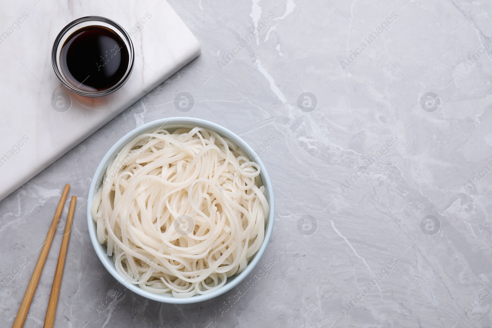 Photo of Bowl of rice cooked noodles and soy sauce served on grey table, flat lay. Space for text
