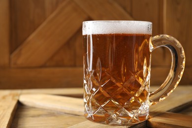 Photo of Mug with fresh beer on wooden crate, closeup. Space for text