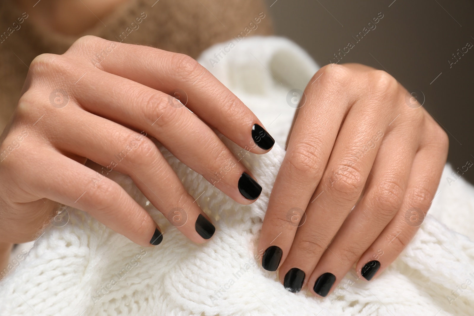 Photo of Woman with black manicure holding knitted fabric, closeup. Nail polish trends