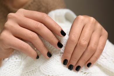 Photo of Woman with black manicure holding knitted fabric, closeup. Nail polish trends