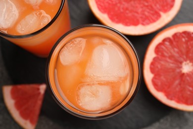 Photo of Tasty grapefruit drink with ice in glasses and fresh fruits on dark table, flat lay