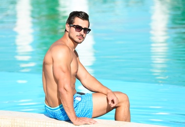 Photo of Handsome young man sitting at swimming pool edge on sunny day