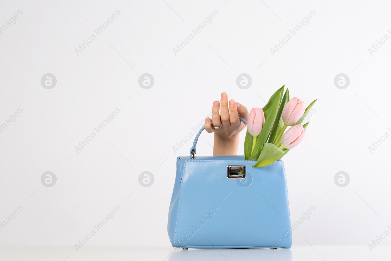 Photo of Woman holding stylish handbag and spring flowers against light background, closeup