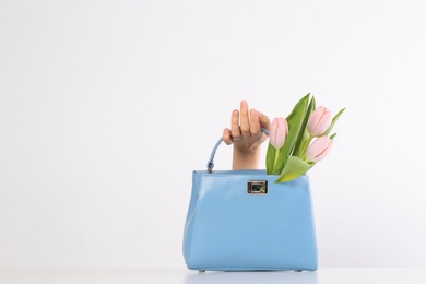 Photo of Woman holding stylish handbag and spring flowers against light background, closeup