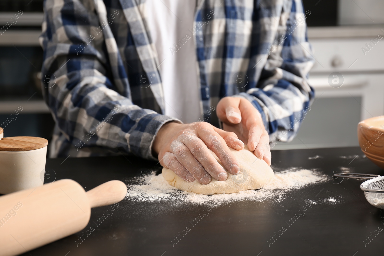 Photo of Man kneading dough on table covered with flour in kitchen