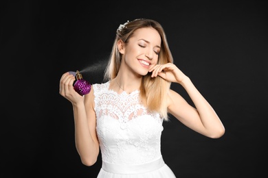 Photo of Beautiful young bride applying perfume against black background