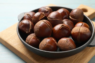 Photo of Fresh edible sweet chestnuts in frying pan on light blue wooden table, closeup