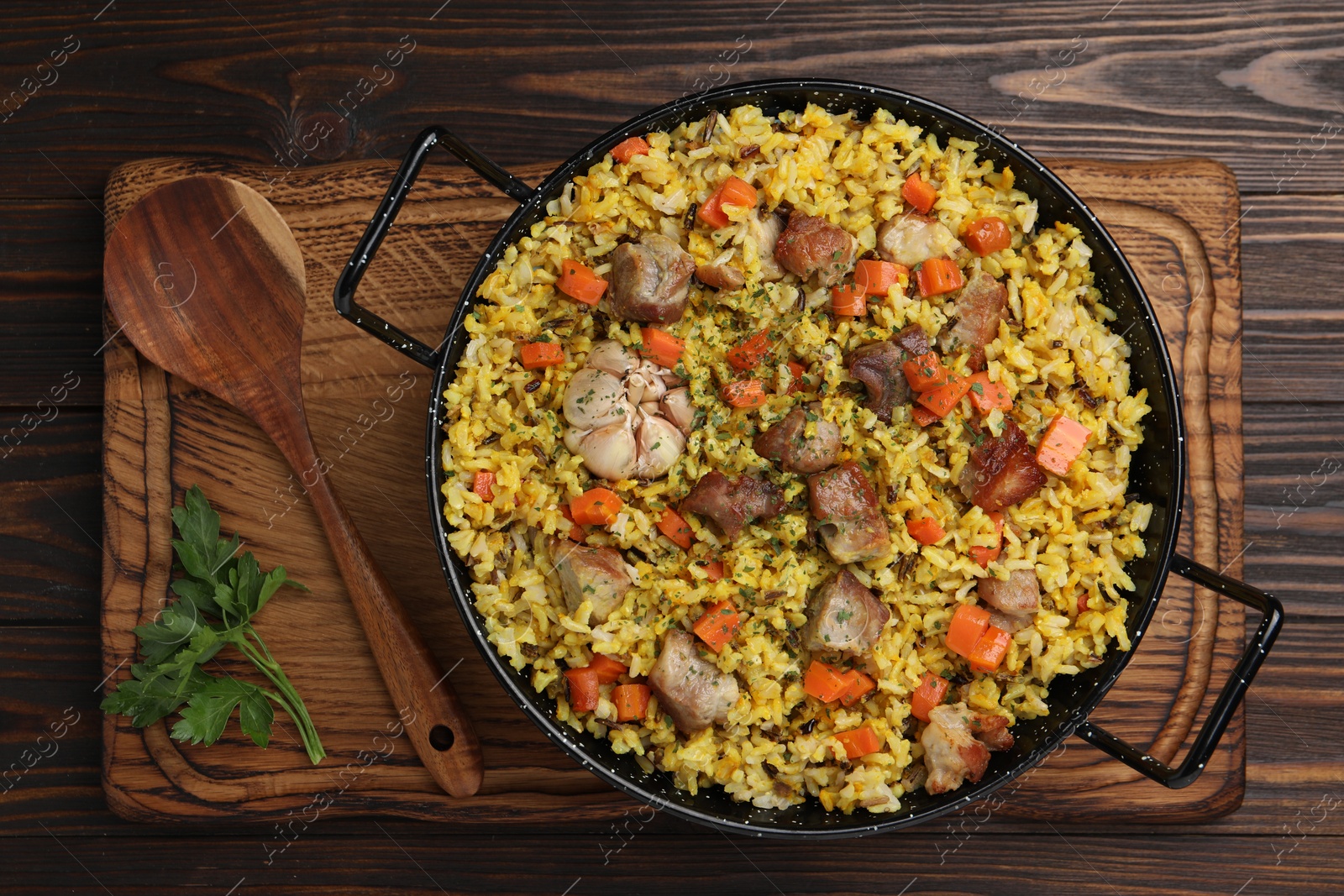Photo of Delicious pilaf with meat, carrot and garlic served on wooden table, top view