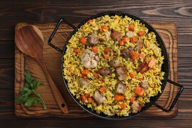 Delicious pilaf with meat, carrot and garlic served on wooden table, top view