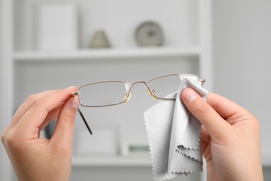 Woman wiping her glasses with microfiber cloth at home, closeup