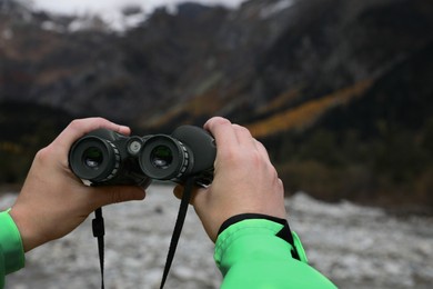 Photo of Woman holding binoculars near river in beautiful mountains, closeup. Space for text