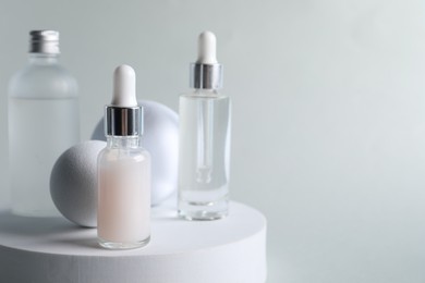 Stylish presentation of bottles with cosmetic serums on light grey background, space for text