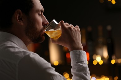 Photo of Handsome man drinking whiskey against blurred lights