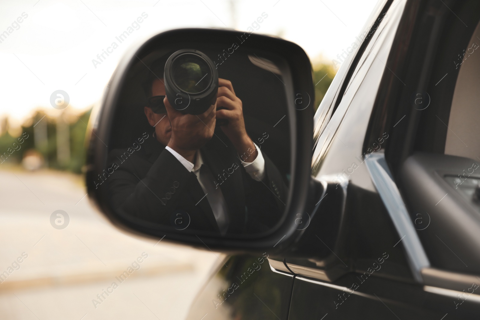 Photo of Private detective with camera spying from auto, view through car side mirror