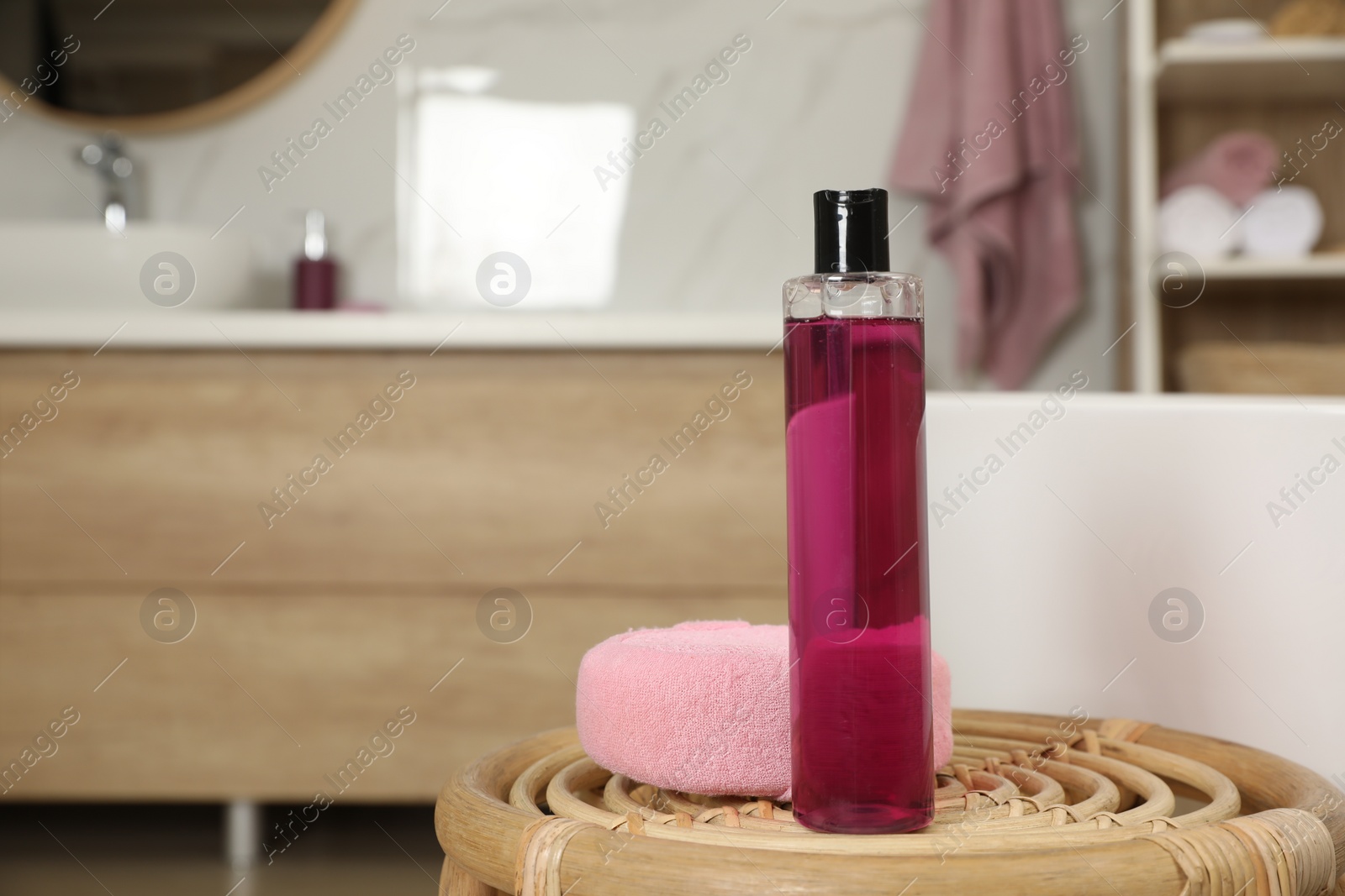 Photo of Bottle of shower gel and sponge on wicker table near tub in bathroom, space for text