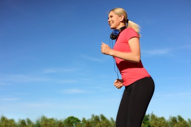 Woman with headphones running outdoors in morning, low angle view. Space for text