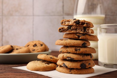 Photo of Stack of delicious chocolate chip cookies and milk on wooden table. Space for text