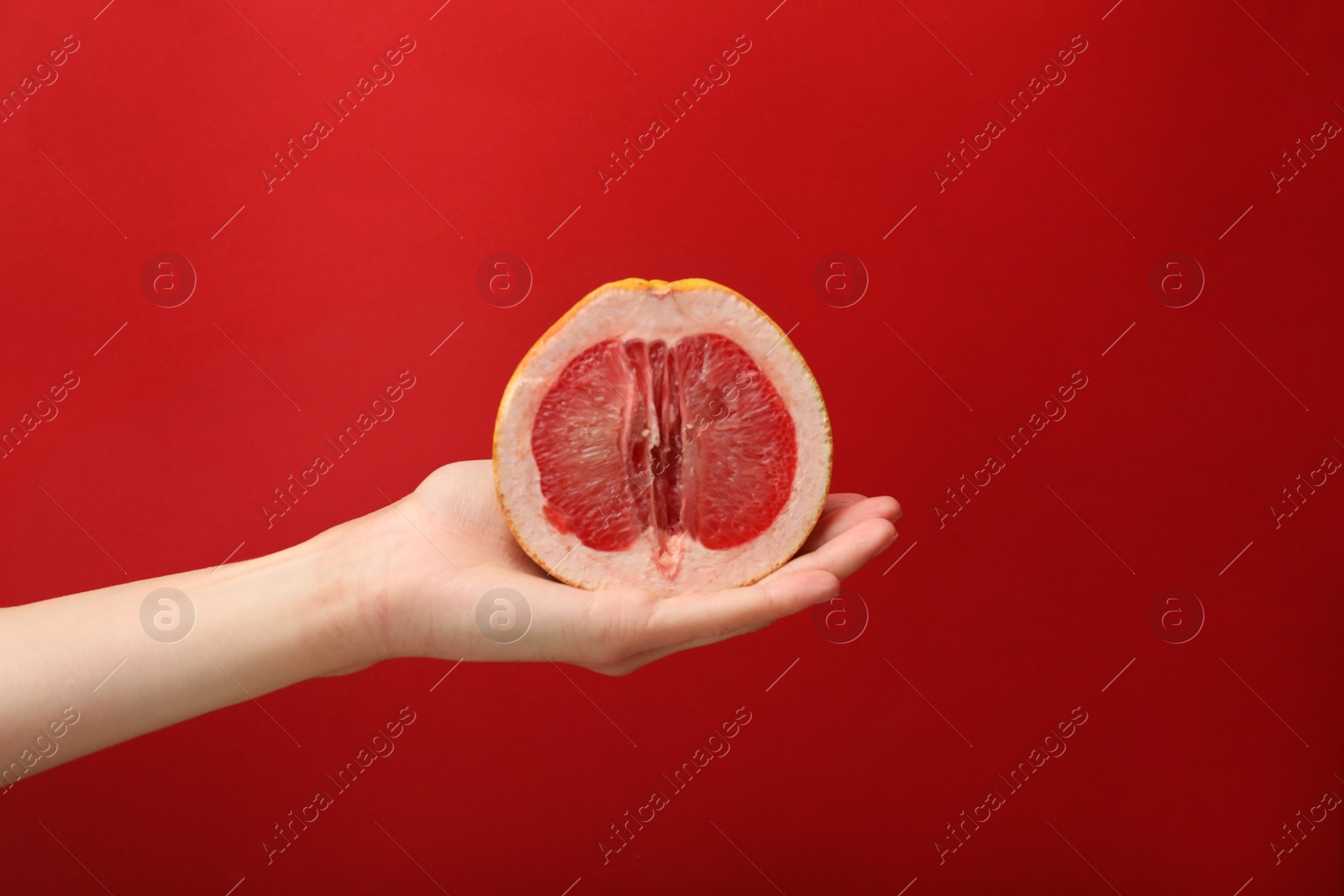 Photo of Woman holding half of grapefruit on red background, closeup. Sex concept