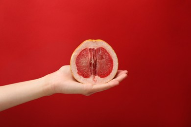 Photo of Woman holding half of grapefruit on red background, closeup. Sex concept