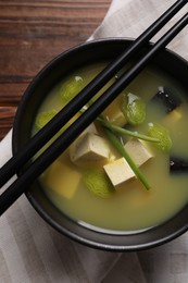 Photo of Bowl of delicious miso soup with tofu and chopsticks served on wooden table, top view