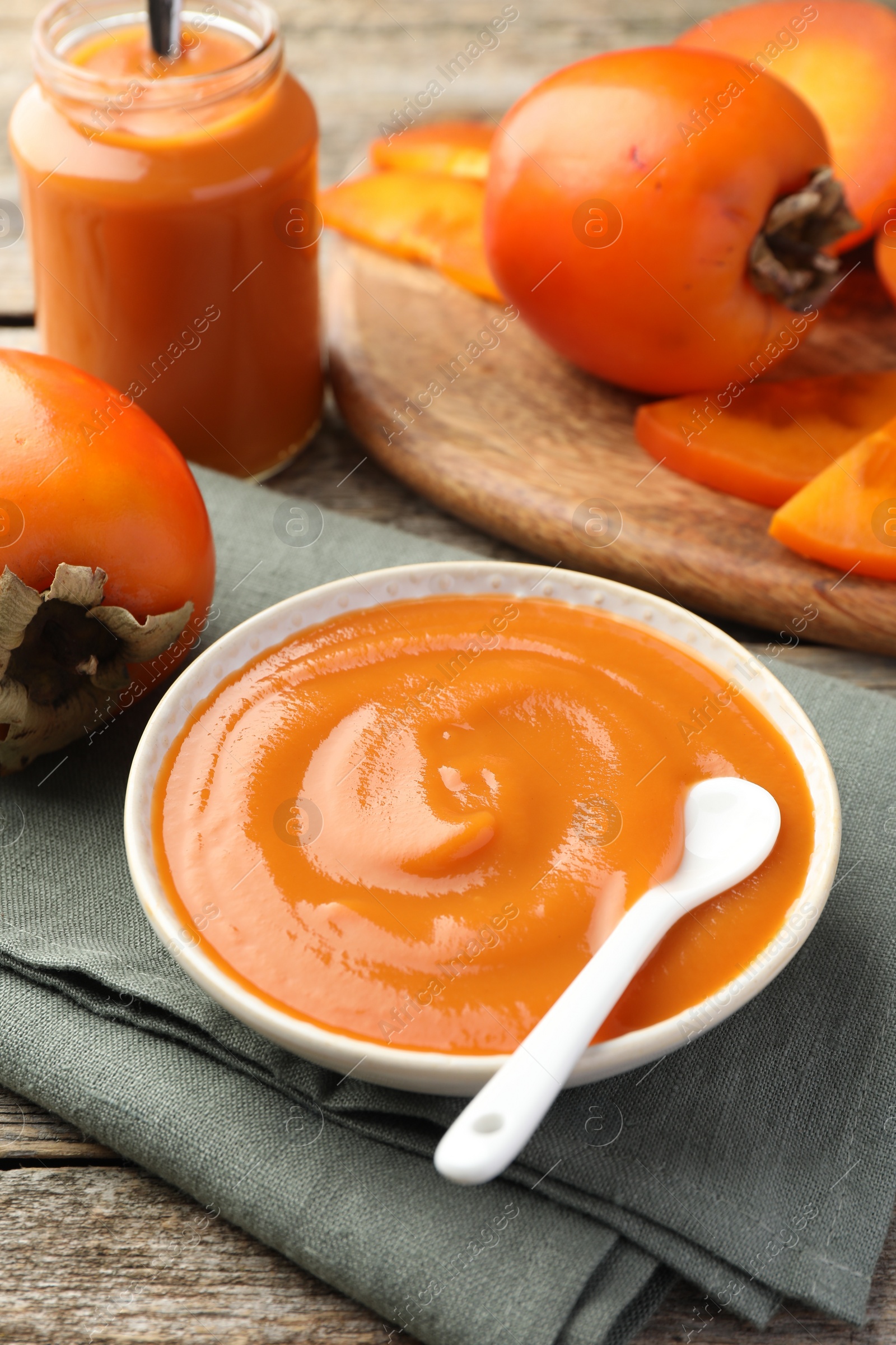 Photo of Delicious persimmon jam and fresh fruits on wooden table