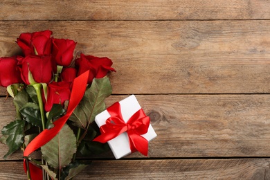 Beautiful red roses and gift box on wooden background, flat lay with space for text. Valentine's Day celebration