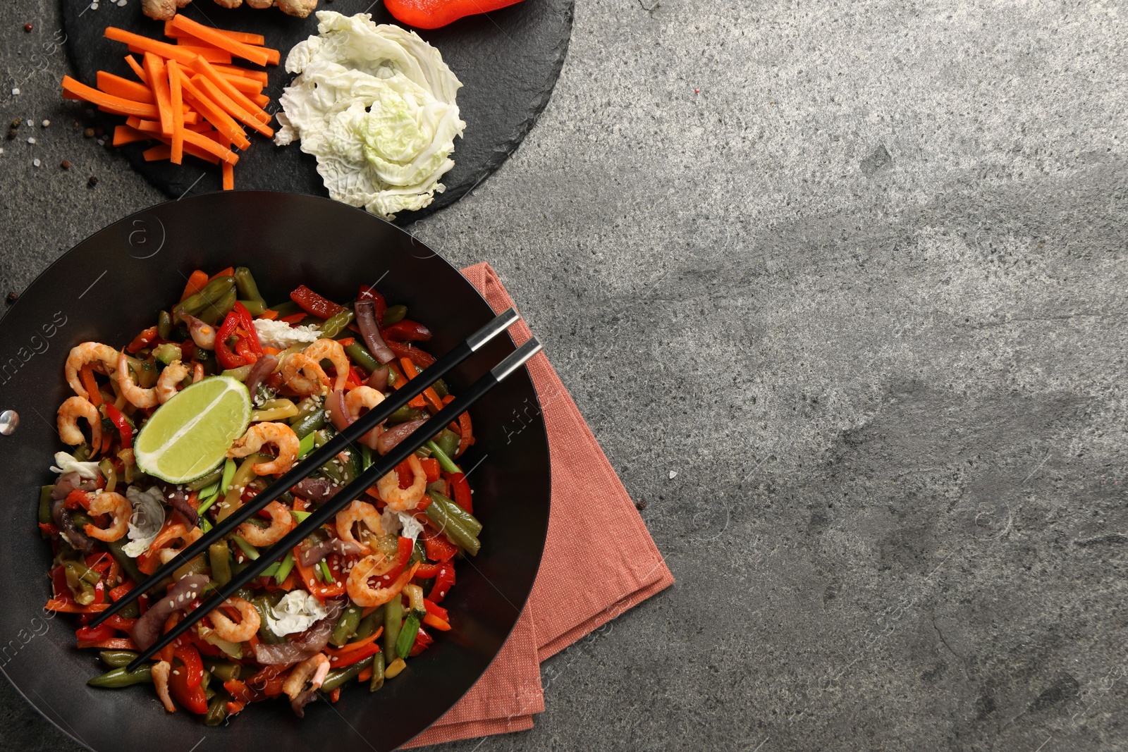 Photo of Shrimp stir fry with vegetables in wok and chopsticks on grey table, flat lay. Space for text