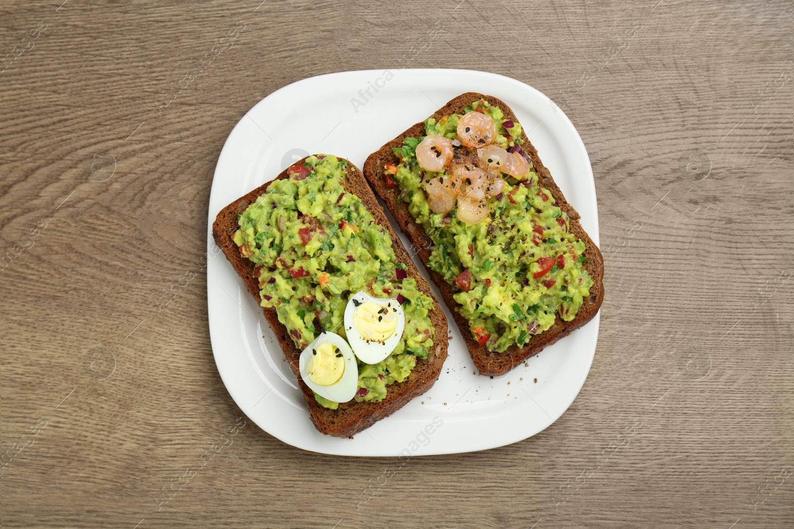 Photo of Slices of bread with tasty guacamole, eggs and shrimp on wooden table, top view