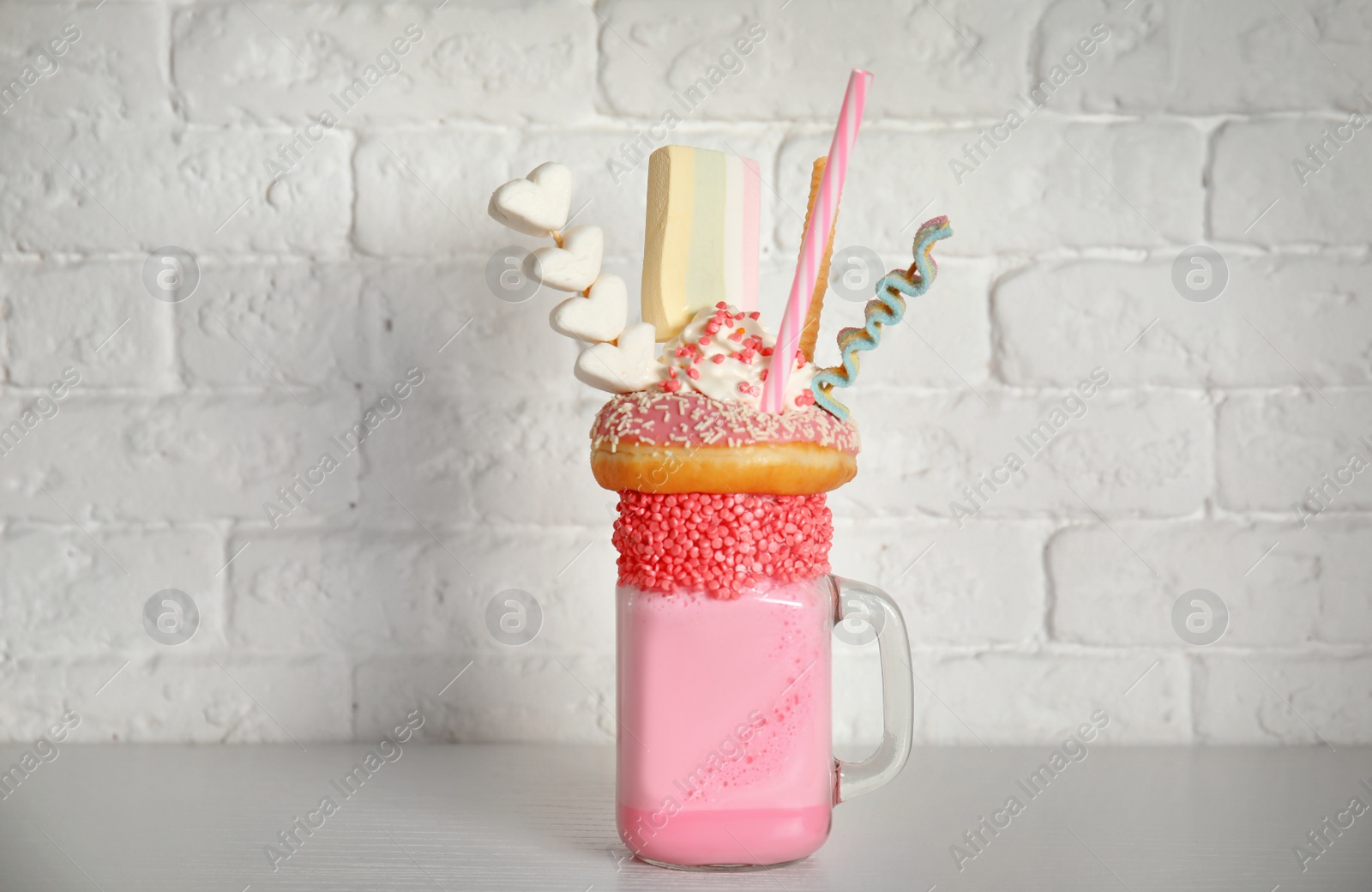 Photo of Tasty milk shake with sweets in mason jar on table near brick wall