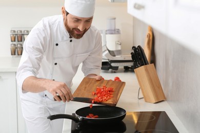 Photo of Happy chef putting cut tomatoes into frying pan indoors