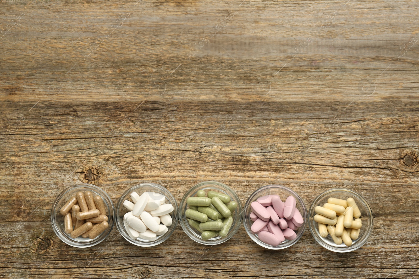 Photo of Vitamin capsules in bowls on wooden table, flat lay. Space for text