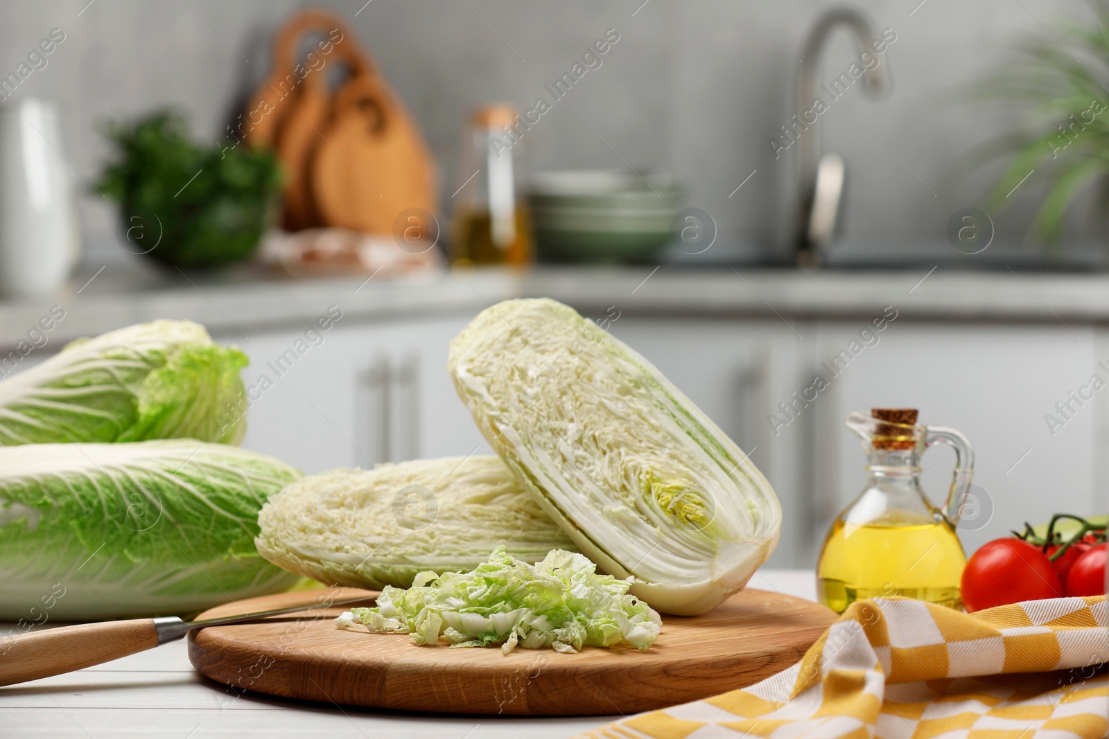 Photo of Fresh Chinese cabbages, knife, tomatoes and oil on white wooden table in kitchen