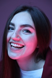 Portrait of smiling woman on purple background in neon lights, closeup