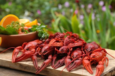 Photo of Delicious red boiled crayfish and products in bowl on wooden table