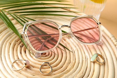 Stylish sunglasses and rings on wicker mat, closeup