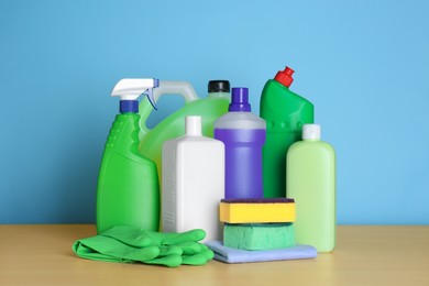 Photo of Different cleaning supplies and tools on wooden table against light blue background