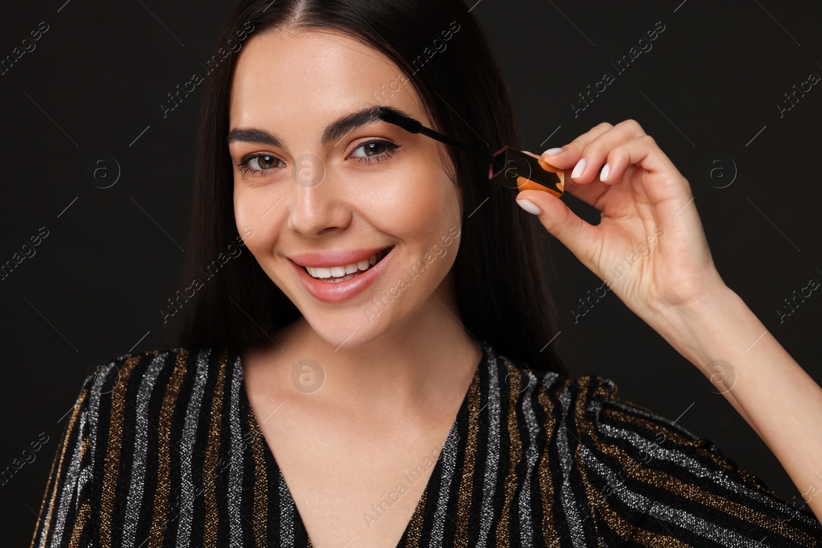 Photo of Beautiful young woman applying mascara on black background, closeup