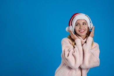Happy woman with headphones on blue background, space for text. Christmas music