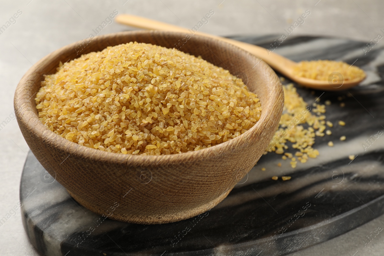 Photo of Raw bulgur in wooden bowl on table, closeup