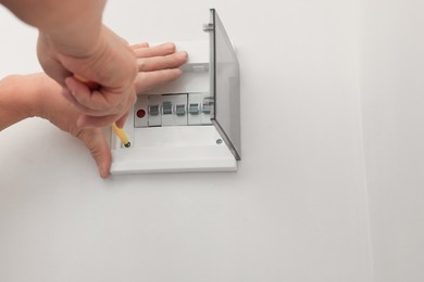 Photo of Electrician installing switchboard with screwdriver indoors, closeup. Space for text