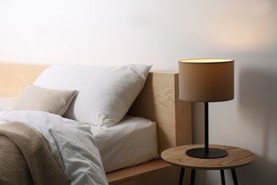Photo of Stylish lamp on table near bed indoors