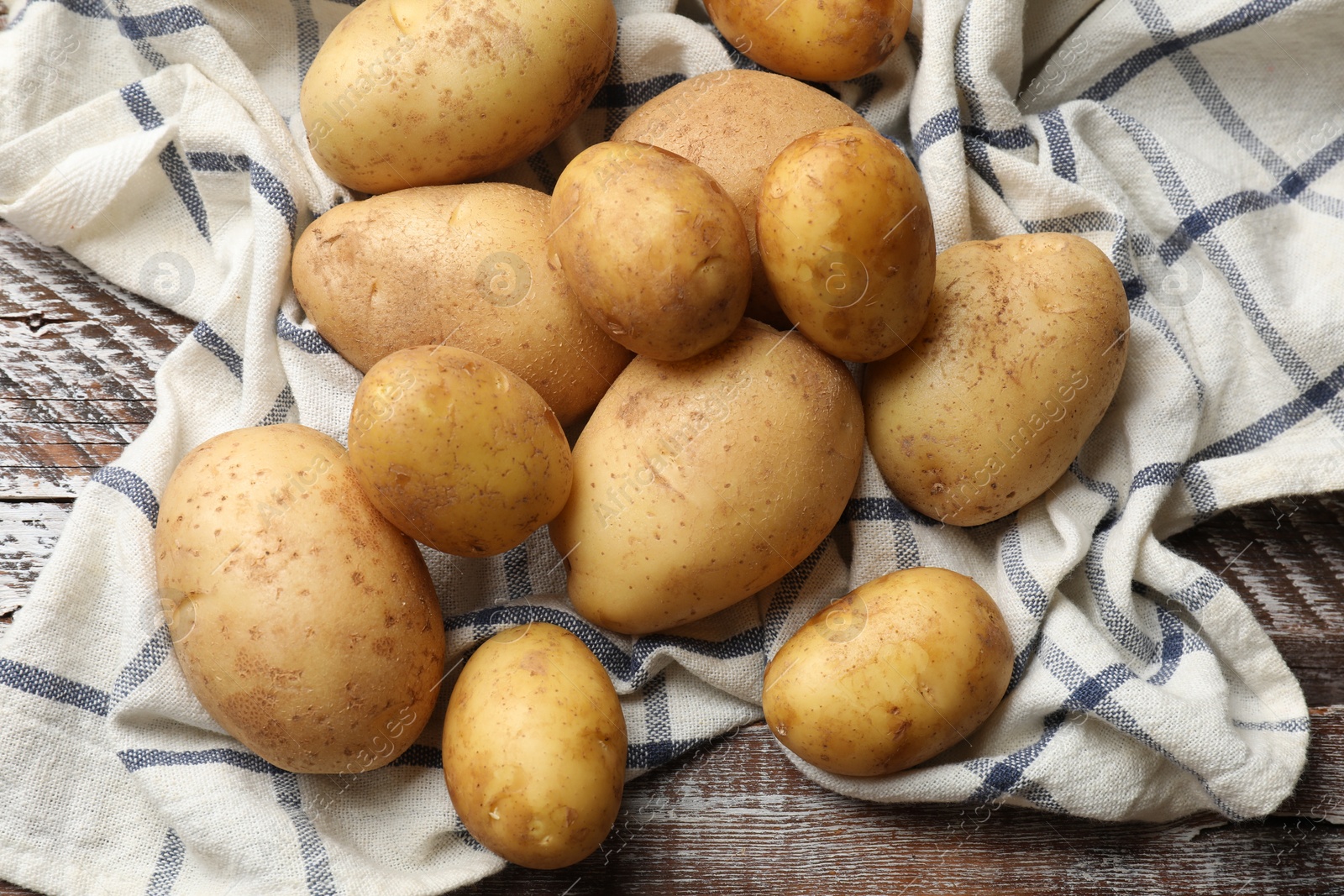 Photo of Raw fresh potatoes and napkin on wooden table, top view