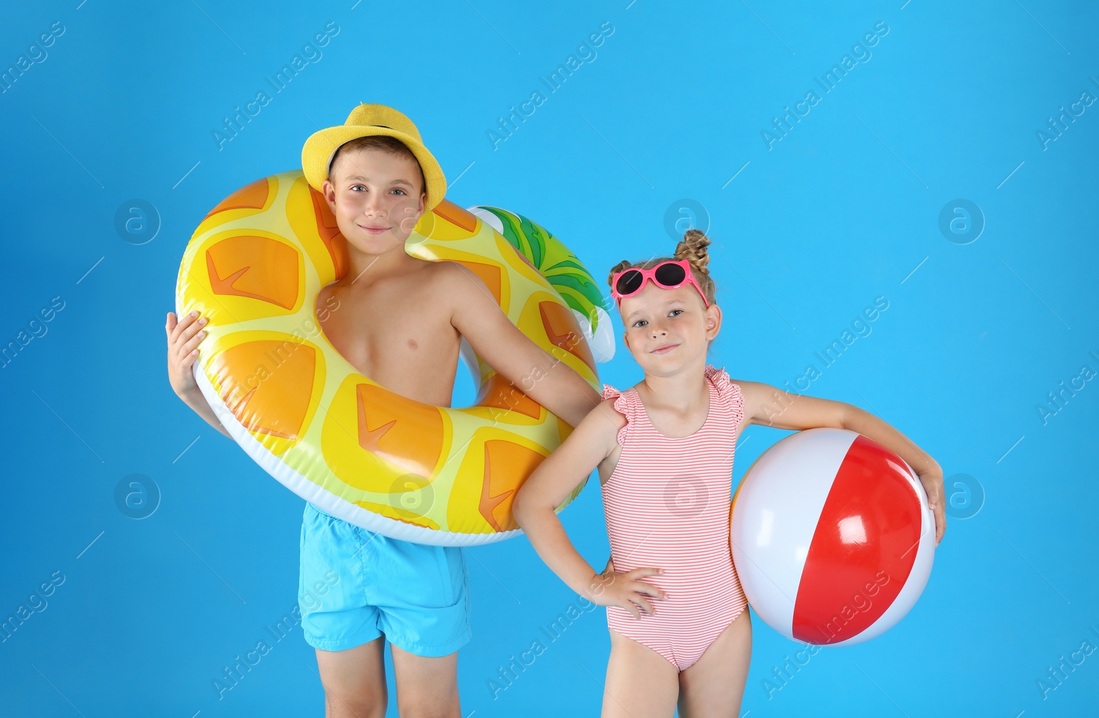 Photo of Cute little children in beachwear with inflatable toys on light blue background