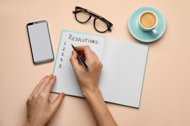 Photo of Woman filling list of new year's resolutions in notebook on beige background, top view
