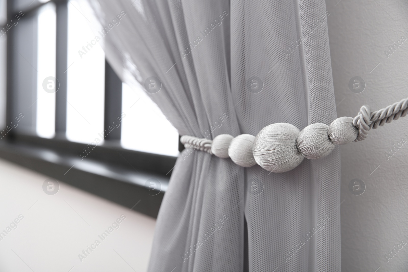 Photo of Beautiful draped window curtain with tieback in room, space for text