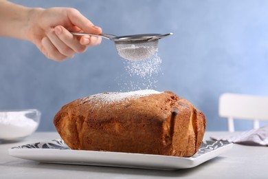 Woman sifting sugar powder onto fresh cake on light table, closeup