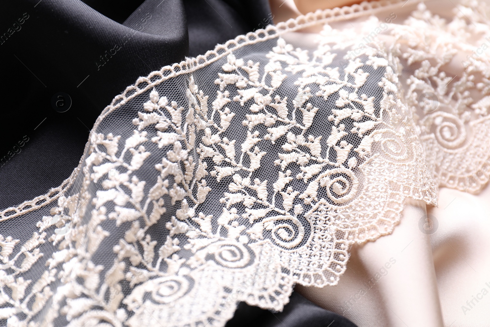 Photo of Beautiful beige lace on color fabrics, closeup