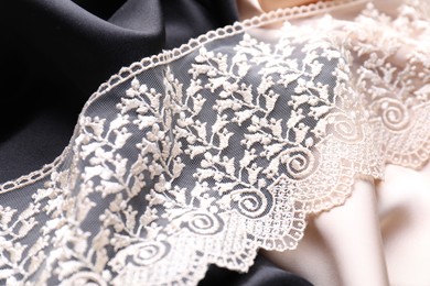 Photo of Beautiful beige lace on color fabrics, closeup