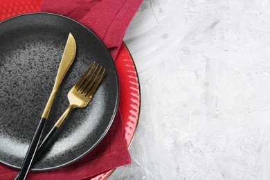 Photo of Clean plates, cutlery and napkin on gray textured table, top view. Space for text