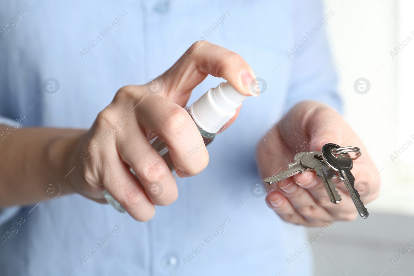 Photo of Woman spraying antiseptic onto keys, closeup view